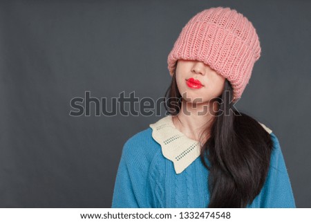 A beautiful Korean girl in a blue sweater and pink hat is wriggling in front of the camera. studio photo shoot, girl posing. hat falls on face
