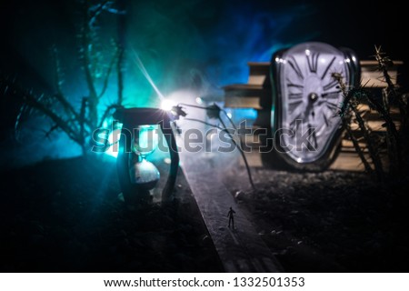 Time concept. Silhouette of a man standing between hourglasses with smoke and lights on a dark background. Surreal decorated picture