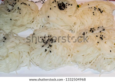 White pasta on a white plate and black sesame seed sprinkled at the top