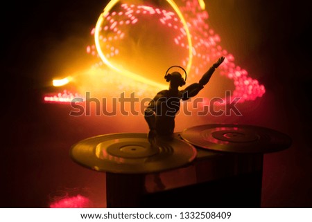 Dj club concept. DJ mixing, and Scratching in a Night Club. Man silhouette on vinyl turntable, strobe lights and fog on background. Creative artwork decoration with toy. Selective focus