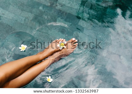 Woman relaxing in swimming pool in Bali luxury resort. Foot spa and skin care lifestyle. Top view photo of legs closeup. Royalty-Free Stock Photo #1332563987