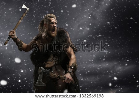 Medieval warrior berserk Viking with tattoo and in skin with axes attacks enemy. Concept photo Royalty-Free Stock Photo #1332569198