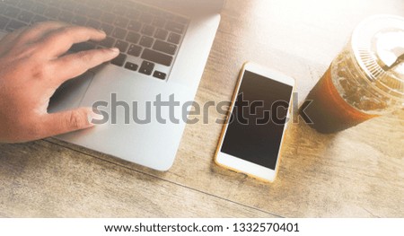 Laptop on a wooden table, hands of a man working on a computer and smartphone