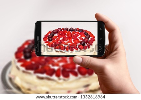Men hands  takes photography of food on table with phone Strawberry cake with cherries and cream. Smartphone photo for post on social networks.