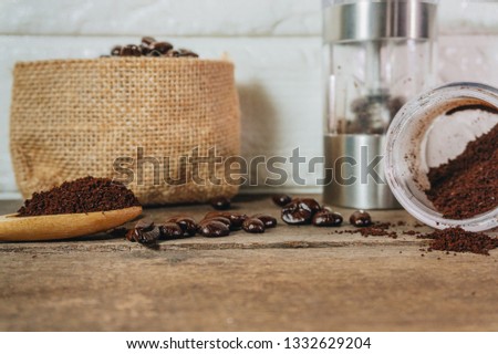 Roasted coffee beans in sacks and crushed coffee with a hand cranked coffee grinder were poured into a spoon on an old wooden table.