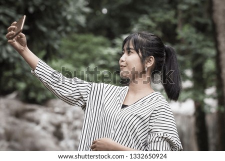 Selfie photo concept : Asian young woman holding smartphone for selfies at  forest, beautiful scenery for peaceful in spring , It shows moisture, tranquility and refreshing of rain forest in Thailand