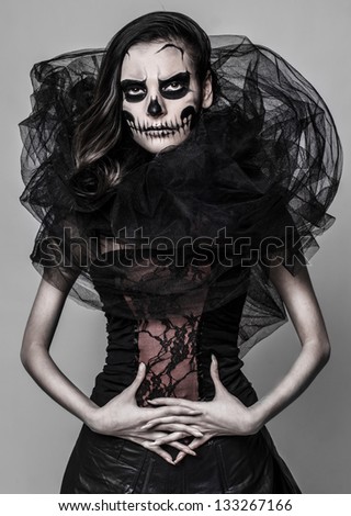 Image of a girl who is posing with a skull mask make up on the grey background