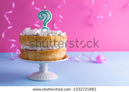 Festive biscuit cake with white cream for a birthday, on a pink and blue background and tinsel and waverki. Question mark candle on the cake.for the holiday. Advertising poster and place for text