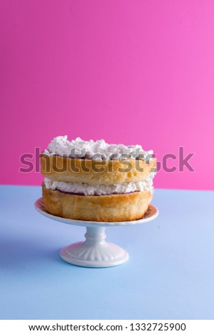 A festive sponge cake with white cream for a birthday, on a pink and blue background. Food for the holiday. Advertising poster and place for text. Copy cpace