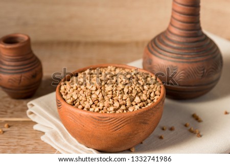 Dry buckwheat in brown clay bowl on wooden table. gluten free grain for healthy diet