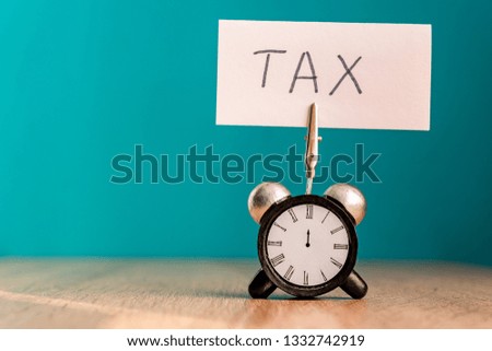 Tax Day Reminder Concept. alarm clock with banner and handwritten word "tax " on wooden table