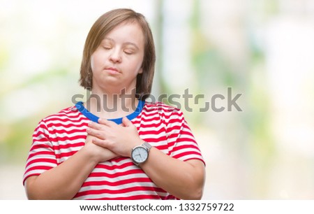 Young adult woman with down syndrome over isolated background smiling with hands on chest with closed eyes and grateful gesture on face. Health concept.