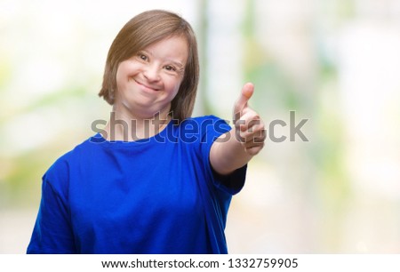 Young adult woman with down syndrome over isolated background doing happy thumbs up gesture with hand. Approving expression looking at the camera with showing success.
