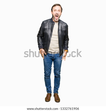 Middle age handsome man wearing black leather jacket In shock face, looking skeptical and sarcastic, surprised with open mouth