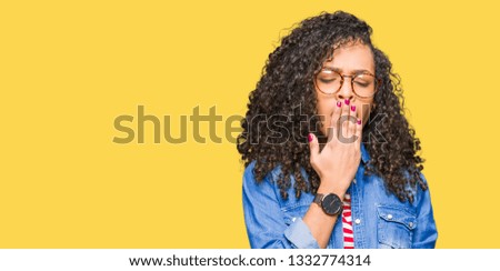 Young beautiful woman with curly hair wearing glasses bored yawning tired covering mouth with hand. Restless and sleepiness.