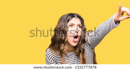 Young beautiful woman wearing stripes sweater Pointing with finger surprised ahead, open mouth amazed expression, something in front