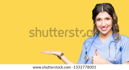 Young adult doctor woman wearing medical uniform Showing palm hand and doing ok gesture with thumbs up, smiling happy and cheerful