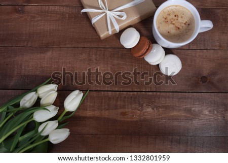 Bunch of white tulips, gifts,  macaroons and cup of coffee on brown  wooden table. Greeting concept. Spring, women or mothers day, cakes, cappuccino