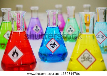 Many of Erlenmeyer flask with colorful solution and Variety type of chemical hazard warning symbols labels. Focus on Biohazard sign,symbol.