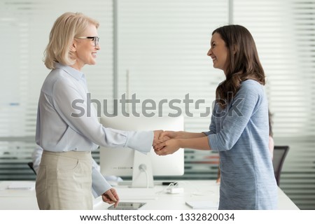 Happy young girl intern student worker get appreciated promoted hired rewarded handshaking helpful female old boss teacher, businesswomen handshake in office as gratitude recognition thanks concept Royalty-Free Stock Photo #1332820034