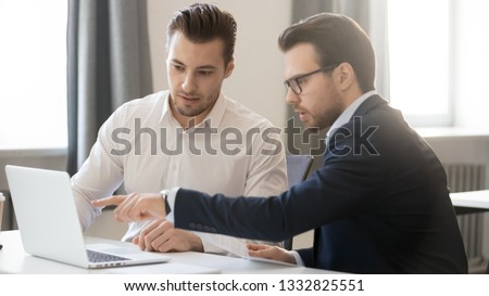 Serious businessman pointing at laptop discussing corporate software with colleague in office, executive male team working together use computer, manager mentor consulting instructing client coworker Royalty-Free Stock Photo #1332825551