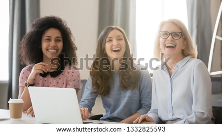 Diverse happy young and old businesswomen laughing looking away engaged in shared corporate meeting, joyful multi-ethnic women different age generation employees sit with laptop having fun at work Royalty-Free Stock Photo #1332825593