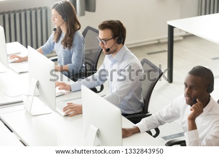 Diverse call center operators team use computers consulting clients in office, multicultural customers service support agents telemarketers in wireless headsets working in open space, view from above Royalty-Free Stock Photo #1332843950