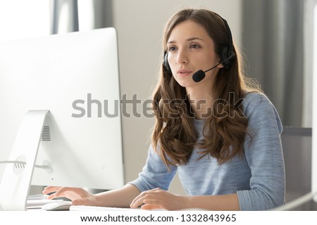 Serious young businesswoman in wireless headset call center agent telemarketer consulting client participating business video conference talk help as customer care service support helpline in office Royalty-Free Stock Photo #1332843965