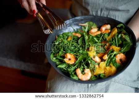 Healthy diet. Salad of arugula, tiger prawns and oranges. Light dish with seafood. Diet menu. Hands interfere salad