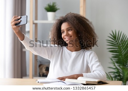 Smiling adolescent schoolgirl distracted from studying learning, african teen raise hand make selfie photo. New generations addicted with gadgets, overuse and dependence of electronic devices concept