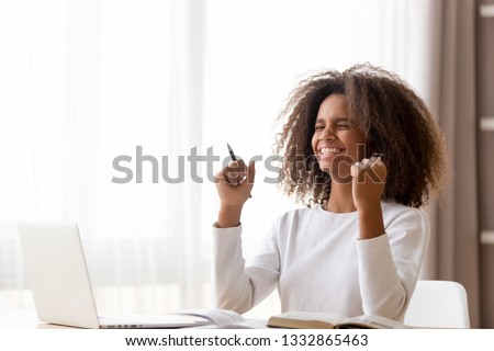 African teen schoolgirl sitting at desk learning studying use pc training materials received great news highest mark successfully pass exams or test at school, accomplish homework feels happy excited Royalty-Free Stock Photo #1332865463