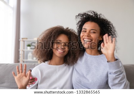 Head shot black teen daughter and mother sitting on sofa look at camera make video call. Older and younger happy american sisters having conversation online via internet waving hands greeting parents Royalty-Free Stock Photo #1332865565