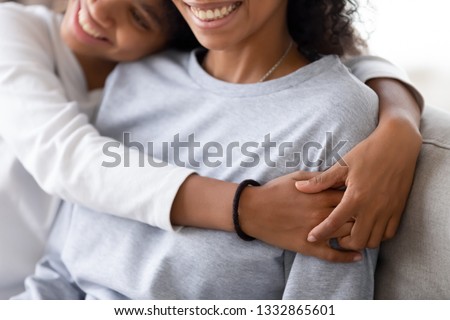 Cropped close up image smiling adolescent daughter cuddling american mom family sitting on couch at home celebrate mother day. Adopted teen child hug new mommy showing love trust and gratitude concept Royalty-Free Stock Photo #1332865601
