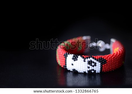 Red bracelet with funny panda on a dark background close up