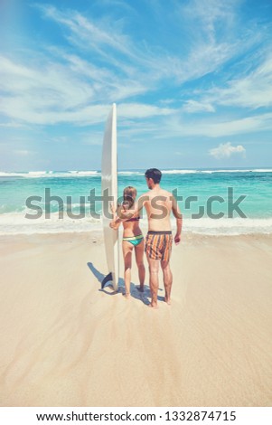 Couple with surfboard enjoying on the tropical beach.
