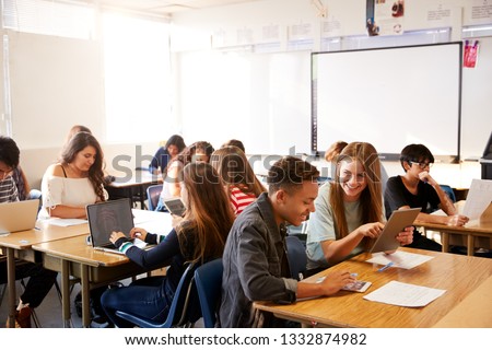 Wide Angle View Of High School Students Sitting At Desks In Classroom Using Laptops Royalty-Free Stock Photo #1332874982