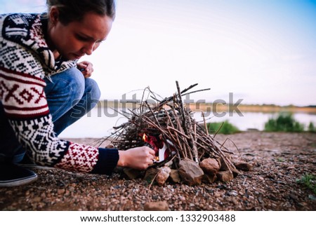 Beautiful girl kindles a bonfire on the river bank