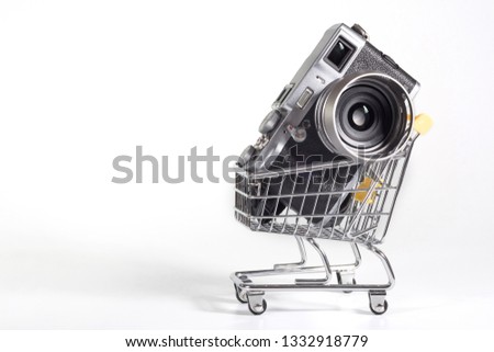 A camera in a small shopping cart at the white background. Selling photo technics, ideas of purchases