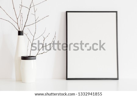 Minimal home decor twigs in a design vase and a poster frame mock up on shelf against white wall.