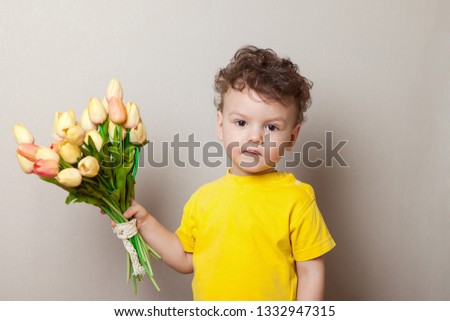 Small boy in a shirt holding a bouquet of tulips and shows thumb up on light background.