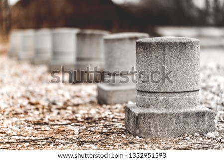 Concrete fence for Parking in the form of round columns with a square base. Installed on a platform covered with small stones.