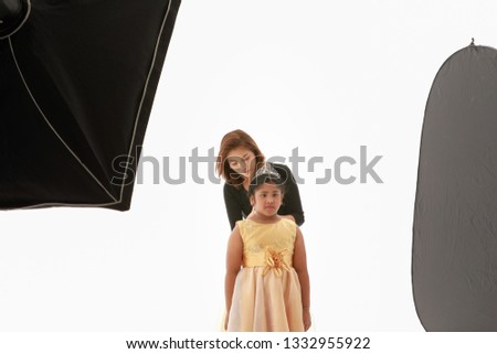 Beautiful Asian stylish assistant helping little girl to pose in studio shooting work among lighting equipments.