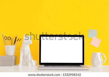 Laptop mockup with geometric decor and supplies on a  desk with yellow wall.