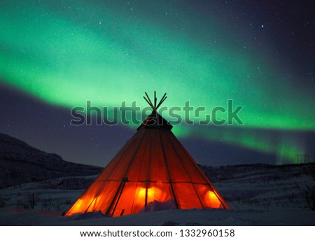 Northern lights over a Sami lavvu. Royalty-Free Stock Photo #1332960158