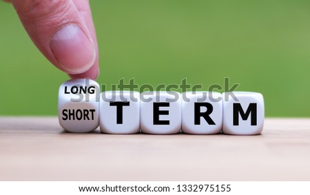 Hand turns a dice and changes the expression "SHORT TERM" to "LONG TERM" (or vice versa). Royalty-Free Stock Photo #1332975155