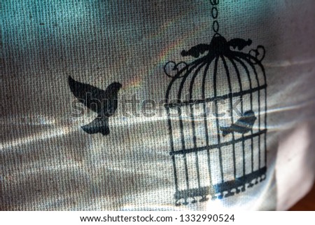 Cloth with the image of a bird, which is sharpened in a cage, with rainbow highlights.