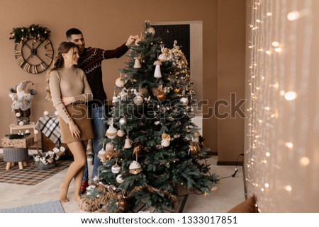 Fancy dressed man and woman in silver gown hug each other tender standing before a Christmas tree