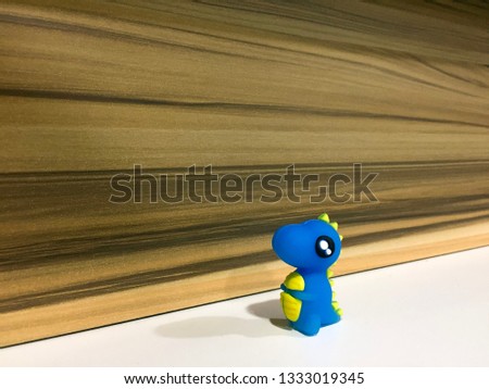 Single blue and yellow color of small miniature dinosaur with white space and wooden background.