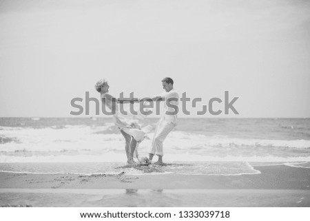 Beautiful happy young wedding Pair of boy and girl in white spinning on ocean beach coast on windy weather sunny day outdoor on blue sky background, horizontal picture