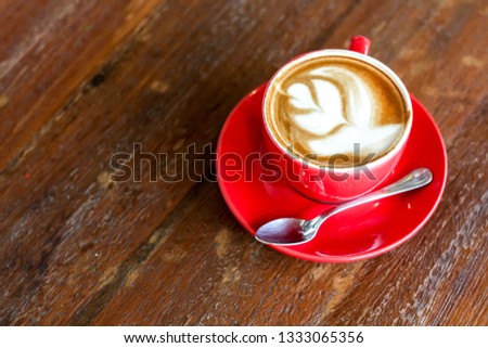 A cup of capuccino latte art heart coffee in red cup on wooden background with copy space.